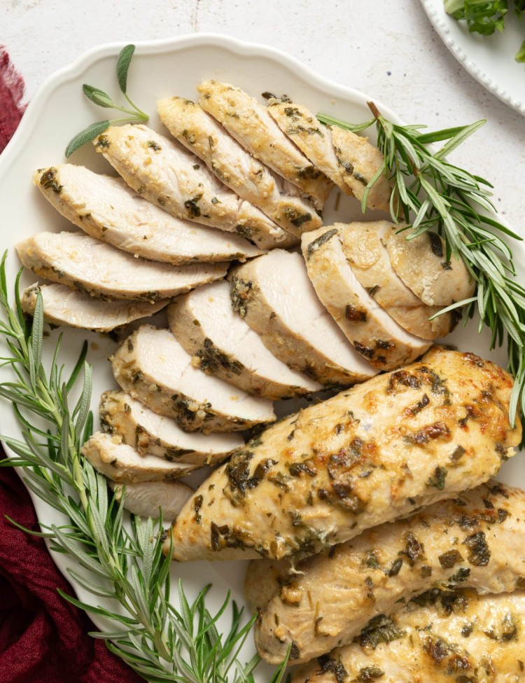 Sliced turkey tenderloin on a serving platter with fresh herbs