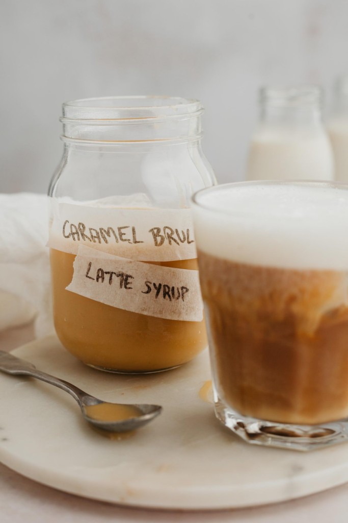 Iced caramel brulee latte next to a jar of caramle brulee latte syrup