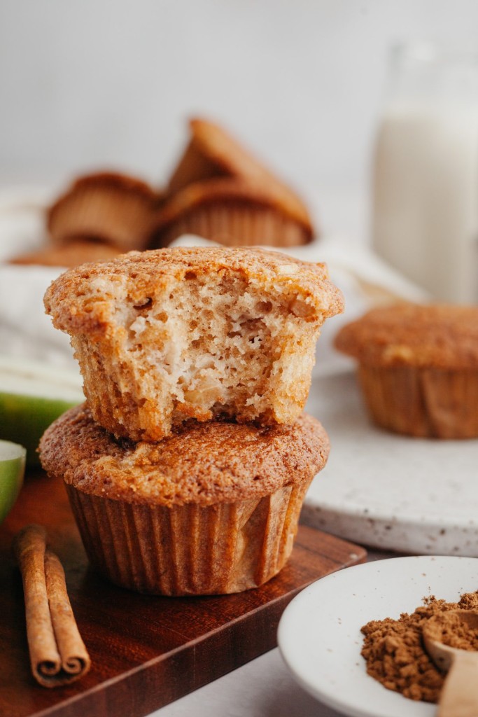 clos up view of cinnamon apple muffins stacked on a plate with a bite out of one