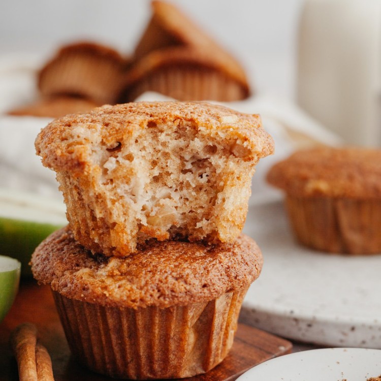 clos up view of cinnamon apple muffins stacked on a plate with a bite out of one