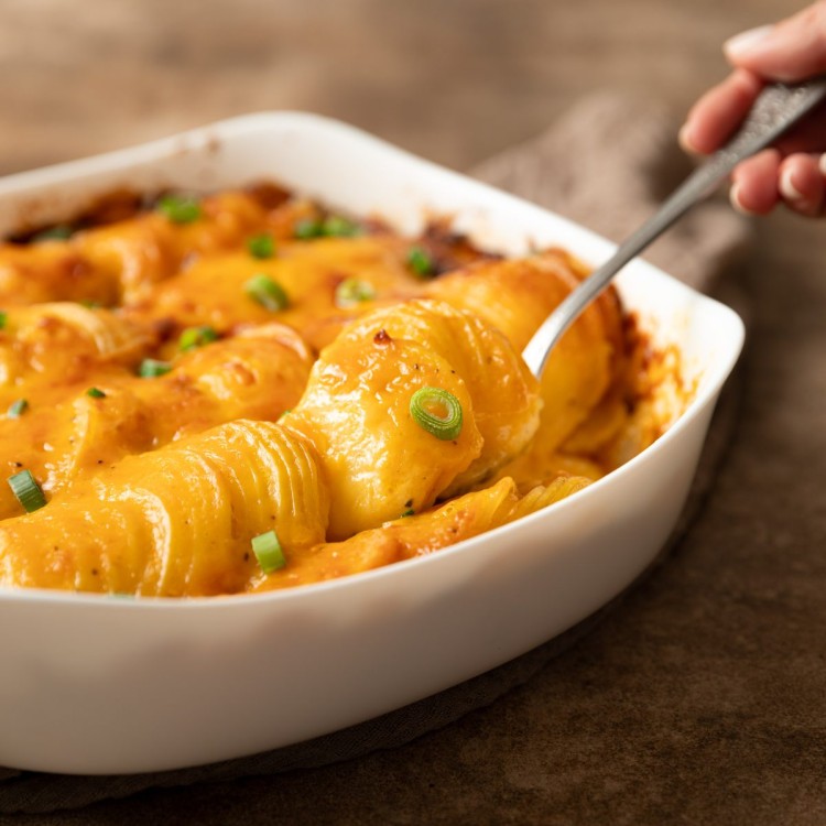 Side view of cheese scalloped potatoes with a spoon pulling a serving out of the casserole dish