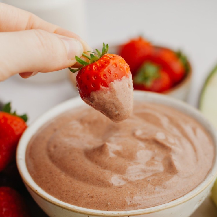 Side view of a strawberry dipping into a bowl of chocolate dip for fruit