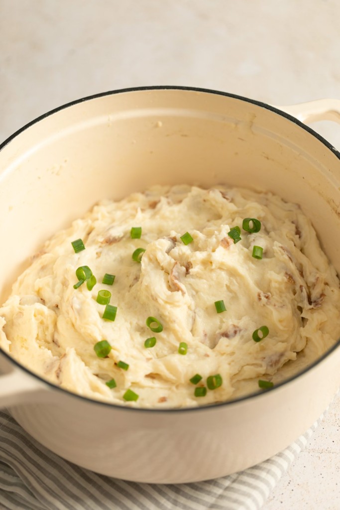 Mashed red potatoes in a white dutch oven garnished with chives
