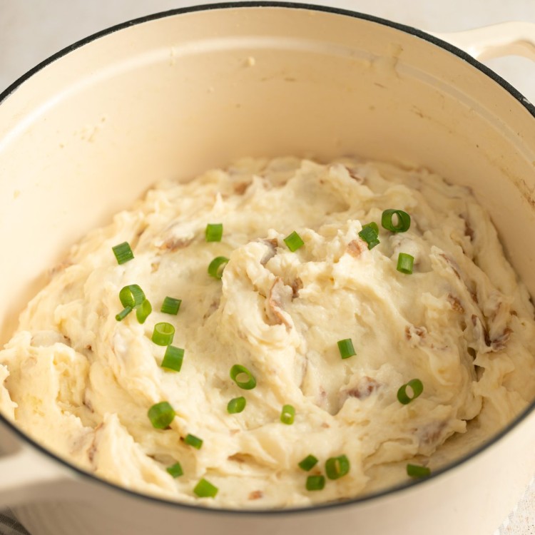 Mashed red potatoes in a white dutch oven garnished with chives