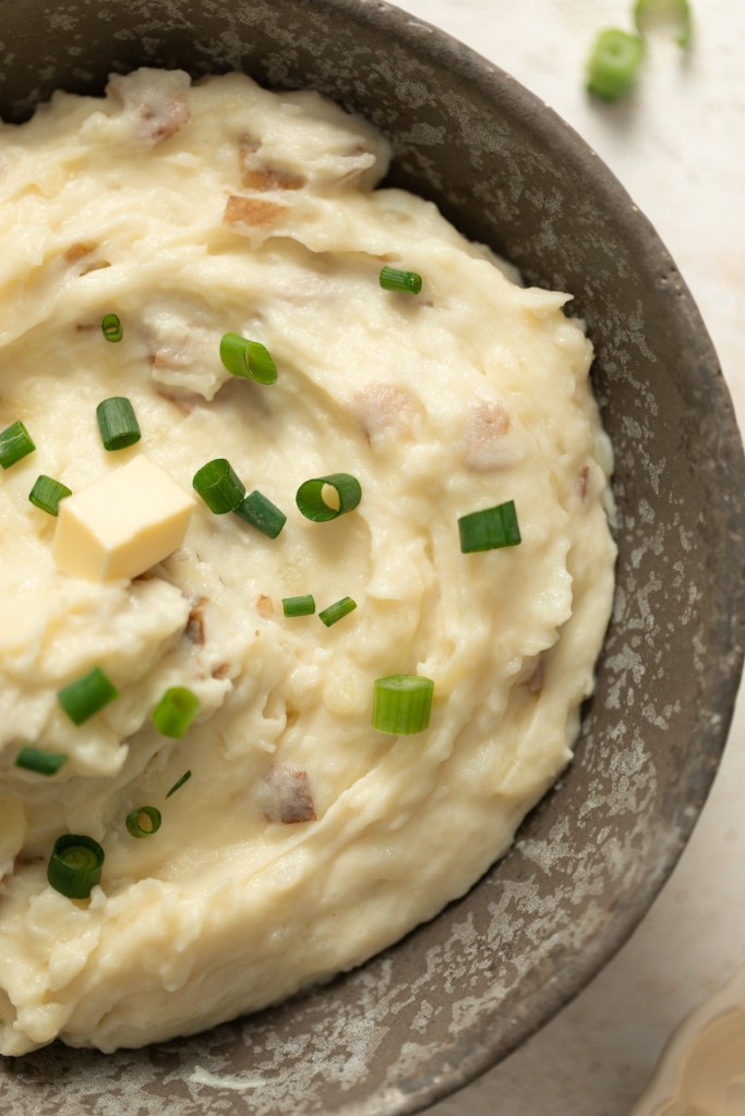 close up of red skin mashed potatoes in a serving bowl with butter and chives as a garnish