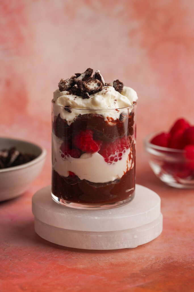 a side view photo of a chocolate parfait in a clear glass with crumbled oreos on top
