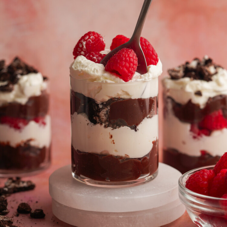 a side photo of chocolate parfait with raspberries on top with a spoon in it and two other parfaits in the backgroun