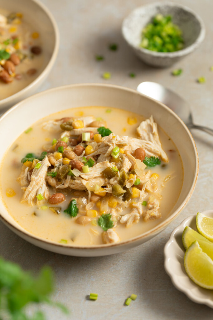 a three quarter photo of white chicken chili in a white bowl with a spoon behind it