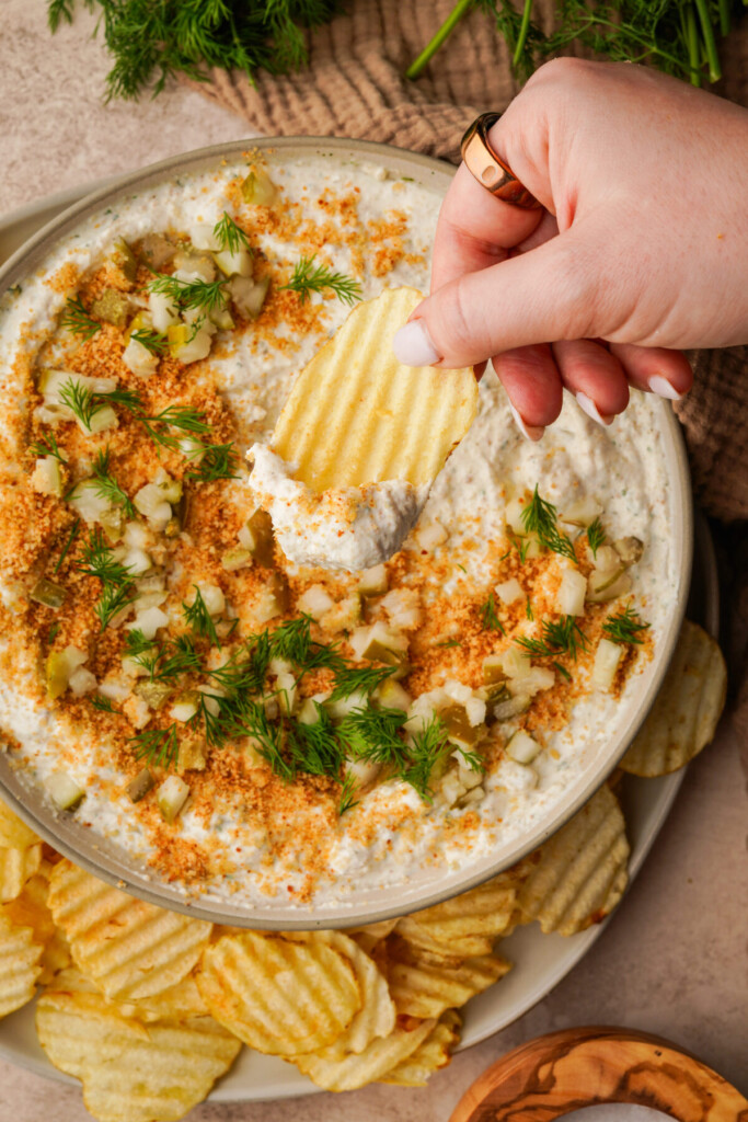 an above image of fried pickle dip with a hand dipping a chip into the dip