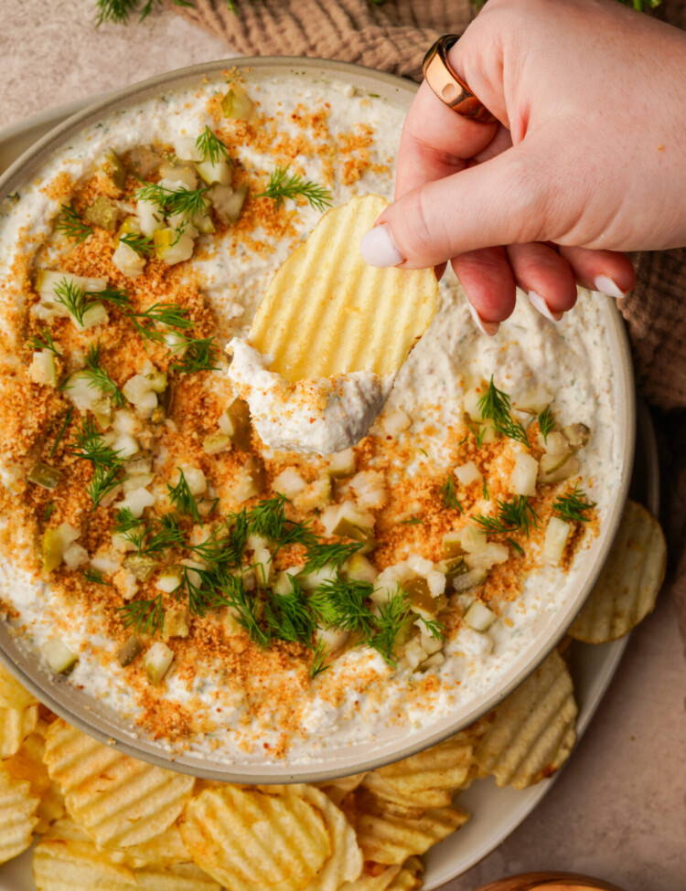 an above image of fried pickle dip with a hand dipping a chip into the dip