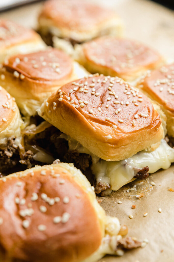 a three quarter view of philly cheesesteak sliders with melted cheese and beef spilling out and one slider pulled away 