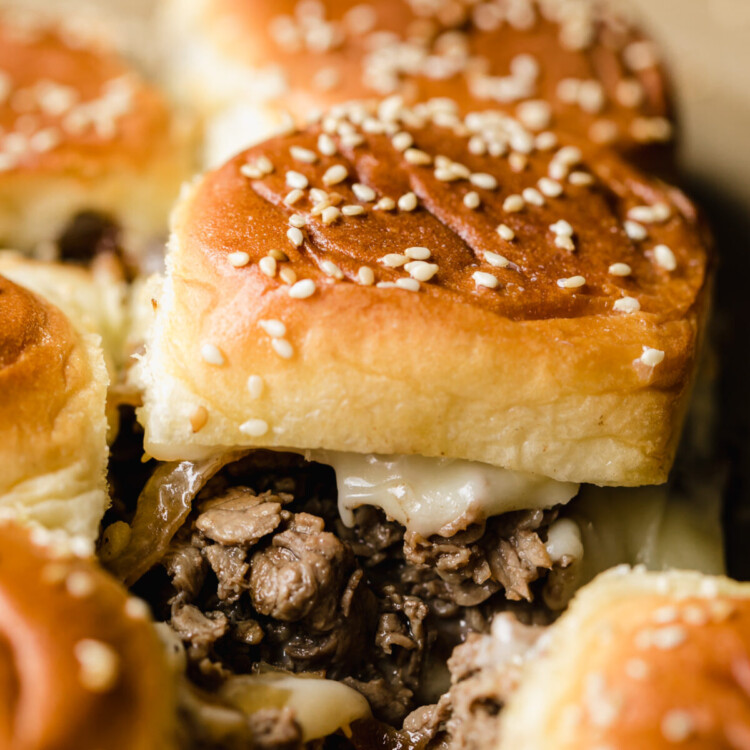 a close up on a philly cheesesteak slider with beef and cheese spilling out the side