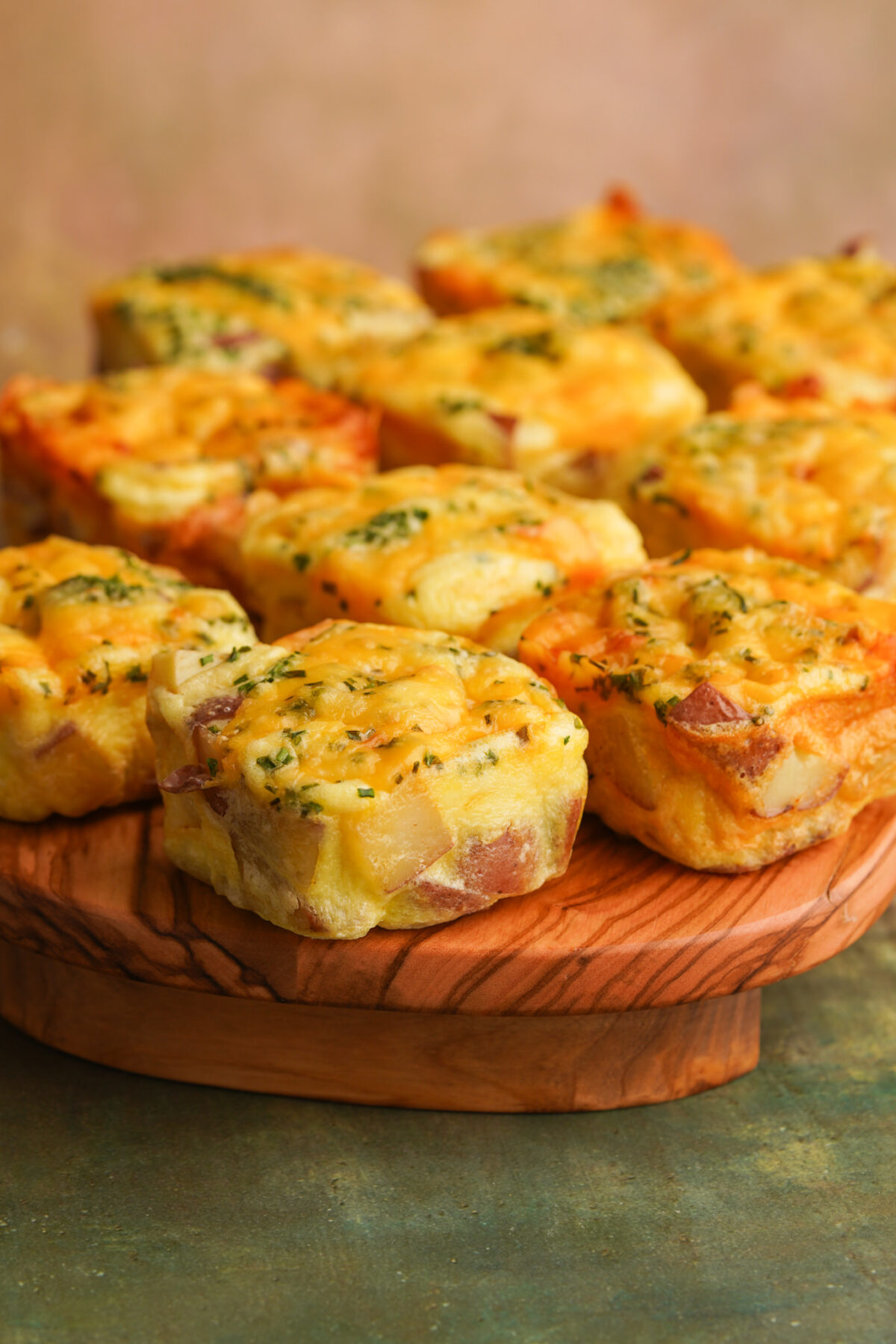 Three quarter view of square potato cheddar and chive egg bakes arranged on a cutting board