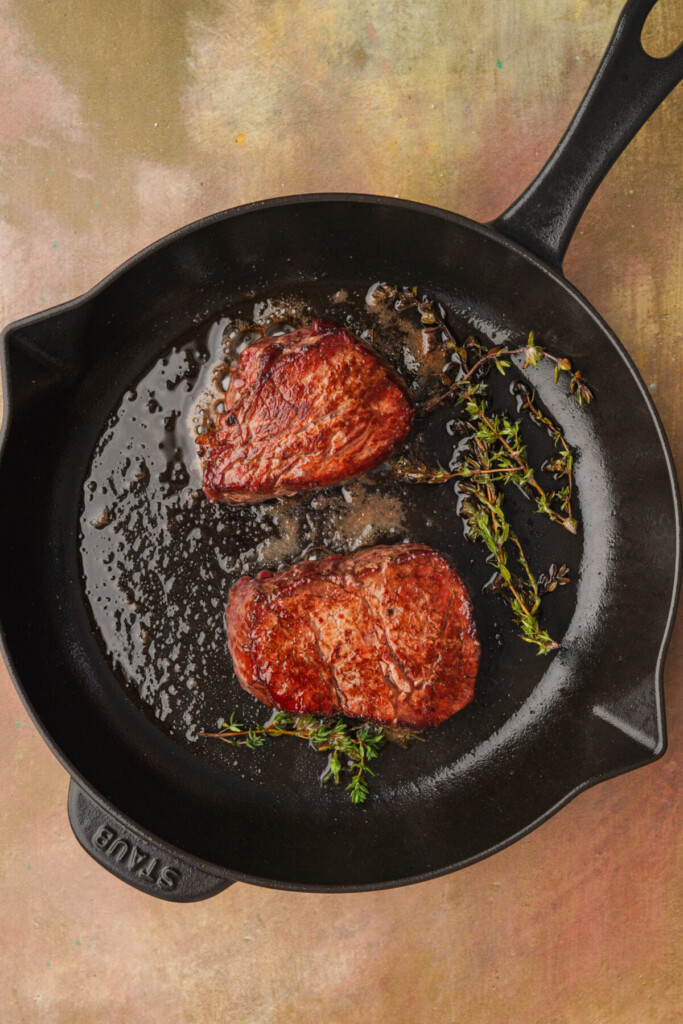 an above photo of two reverse sear filet mignons in a cast iron with thyme