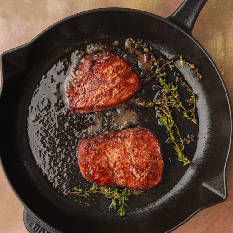 an above photo of two reverse sear filet mignons in a cast iron with thyme