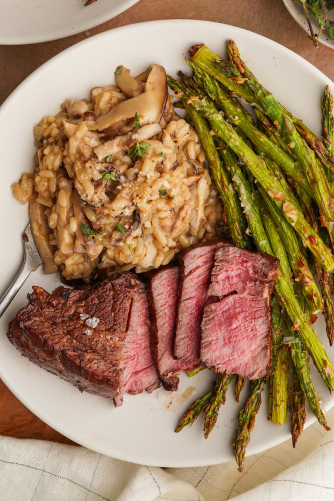 a close up photo on a plate with sliced filet mignon, truffle mushroom risotto and air fryer asparagus