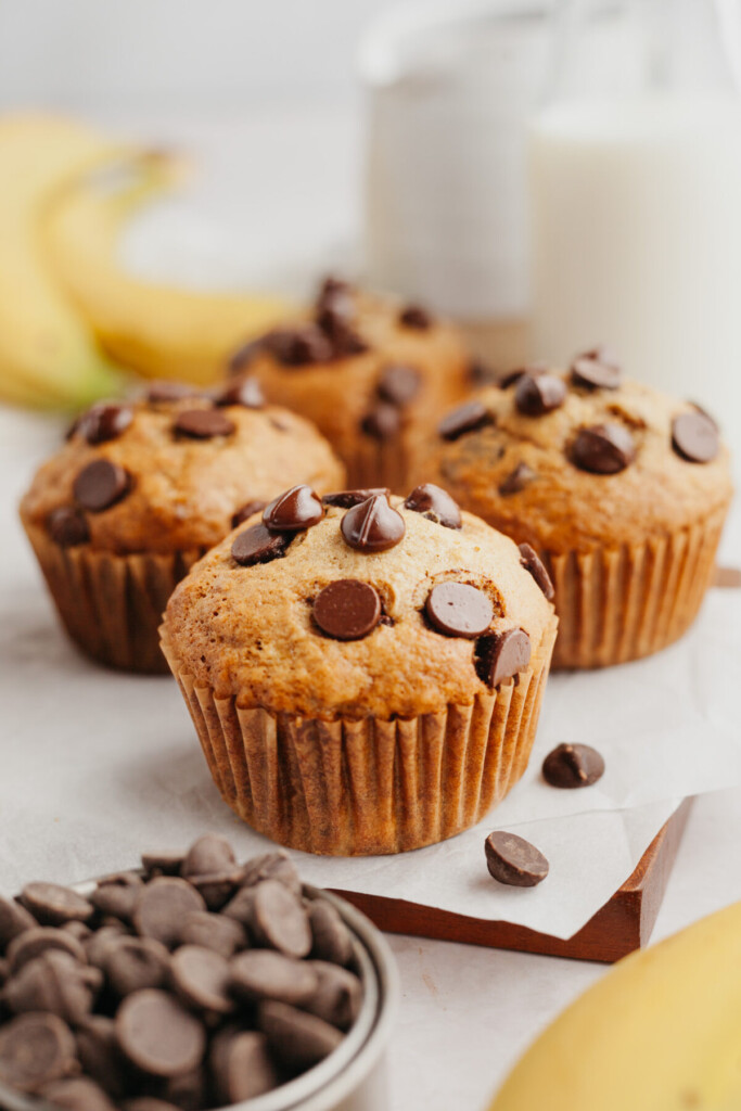 a side view photo of four banana muffins with chocolate chips on a cutting board lined with parchment paper