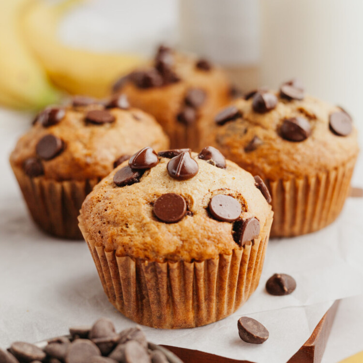 a side view photo of four banana muffins with chocolate chips on a cutting board lined with parchment paper
