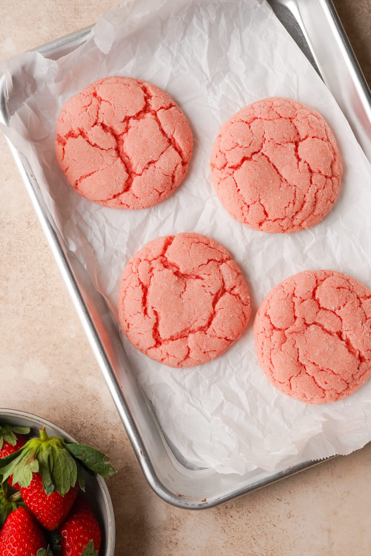 Above view of strawberry cookies with a crinkled top on a parchment line baking sheet