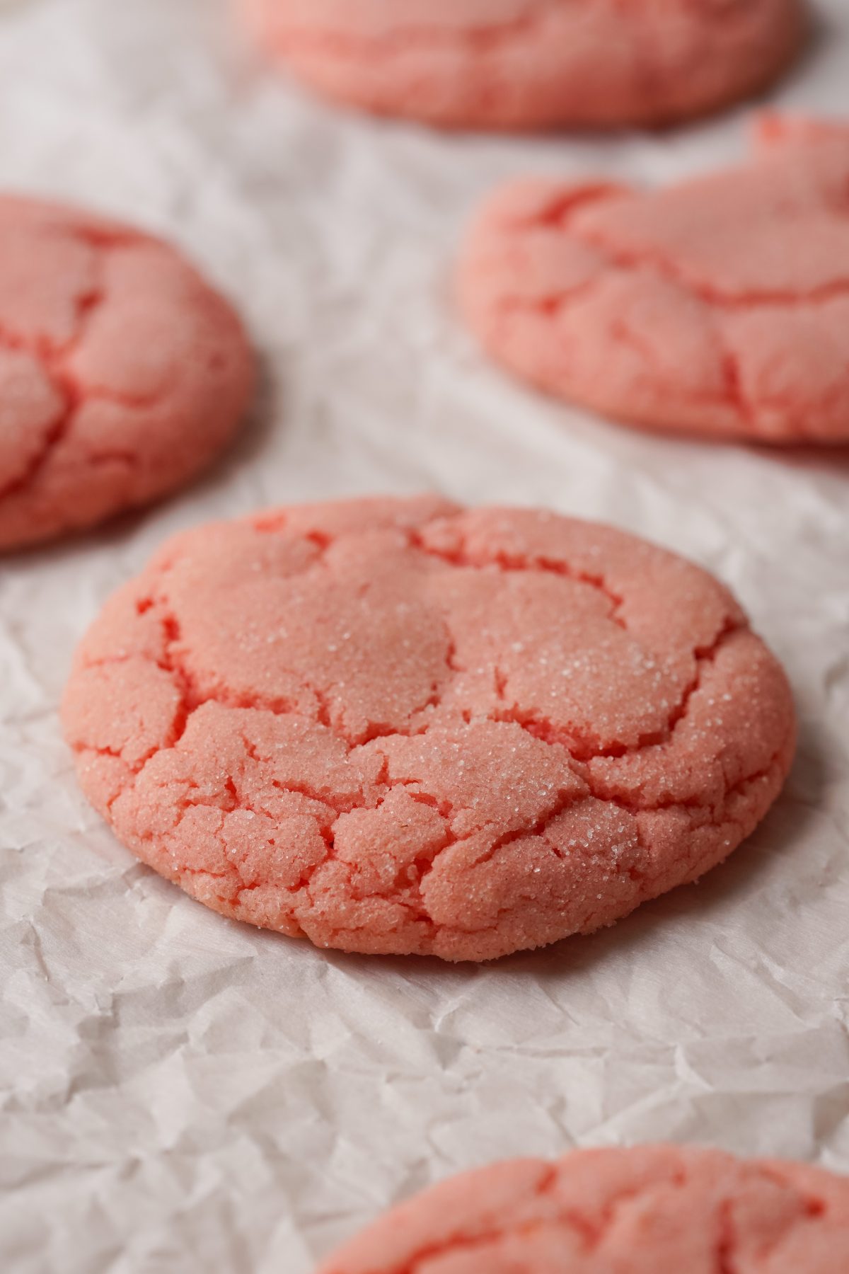 Three quarter view of strawberry cookies with a crinkle top on a piece of parchment