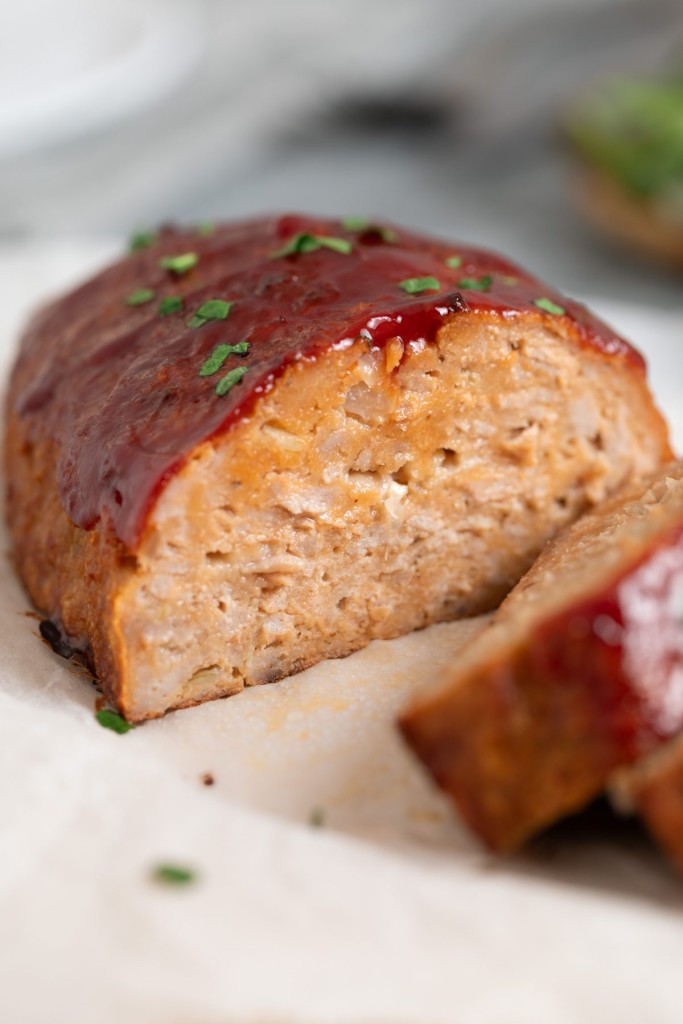 Three quarter view of a turkey meatloaf partially sliced on a cutting board with parchment paper