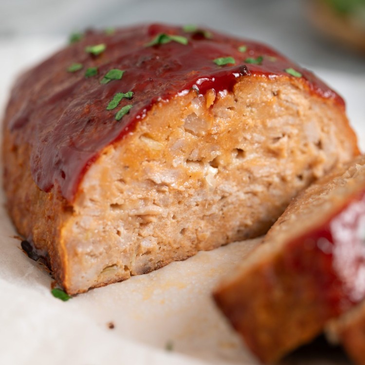 Side view of a turkey meatloaf partially sliced on a cutting board with parchment paper