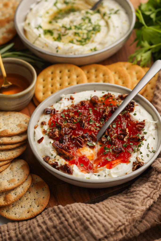 a three quarter view photo of goat cheese dip with jam on top with crackers around it