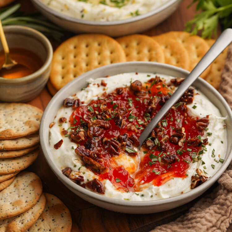 a three quarter view photo of goat cheese dip with jam on top with crackers around it