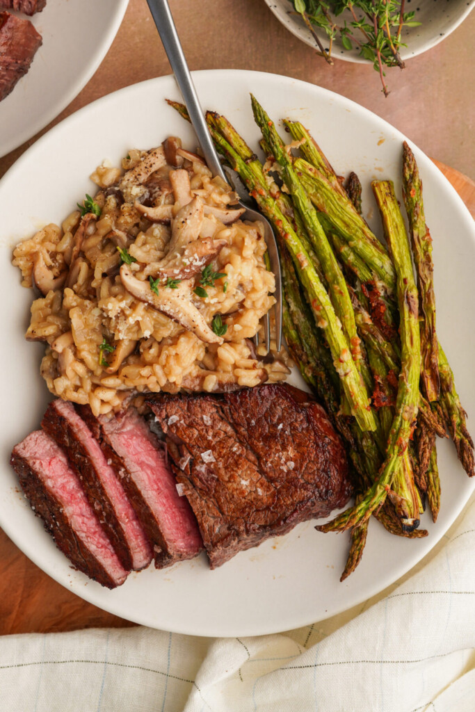 an above photo of air fryer asparagus on a plate with slices of steak and mushroom risotto
