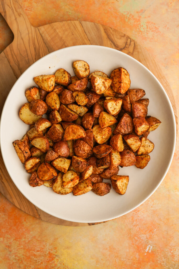 an above image of air fryer red potatoes in a white bowl on a round wooden cutting board