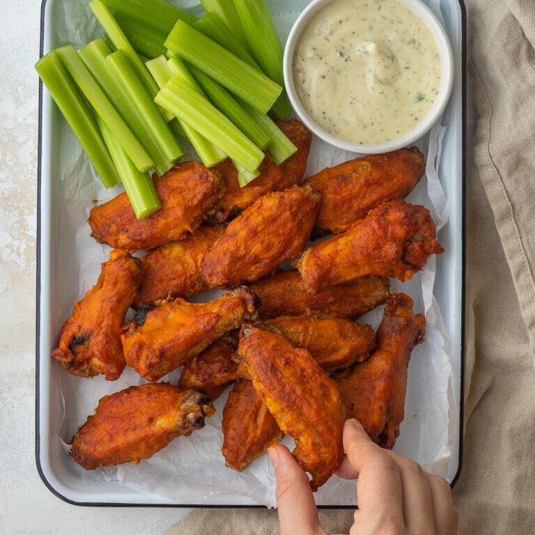 a photo of carolina gold bbq wings on a tray with celery sticks and a small bowl of ranch dressing