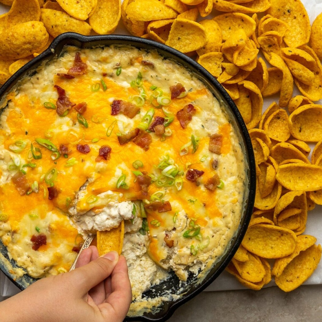 a photo of bacon ranch chicken cheese with a hand dipping a corn chip into the dip