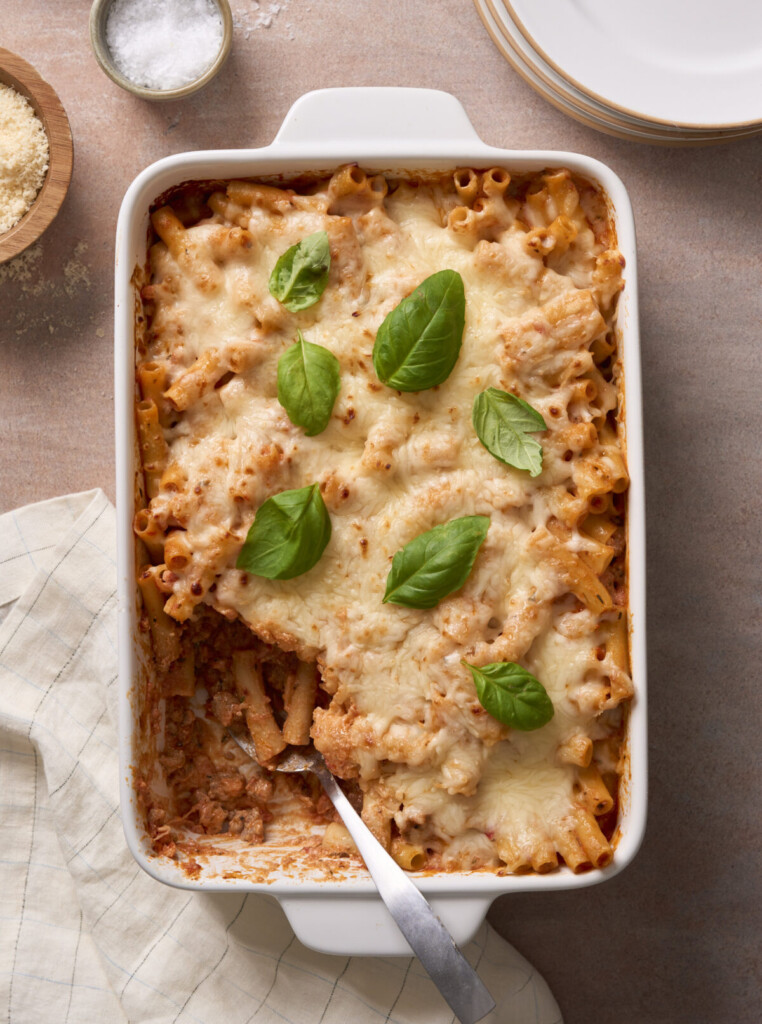 an above view image of baked ziti with ricotta in a casserole dish with a serving taken out and a spoon resting in it