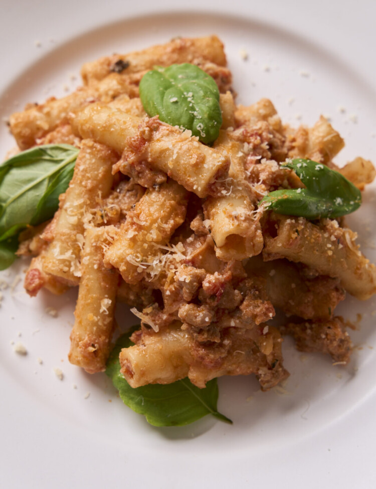 a close up photo of the baked ziti on a white plate with parmesan and basil on top