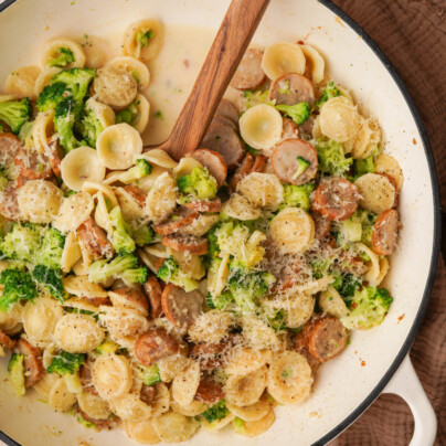 an above view photo of a pot of broccoli sausage pasta with a wooden spoon in it