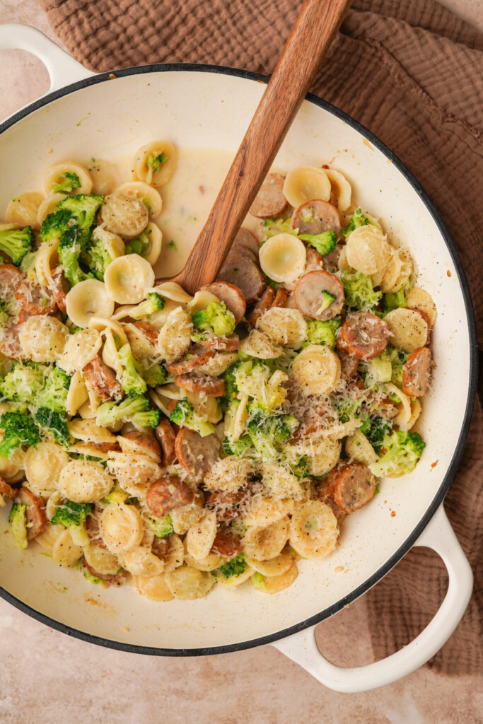 an above view photo of a pot of broccoli sausage pasta with a wooden spoon in it