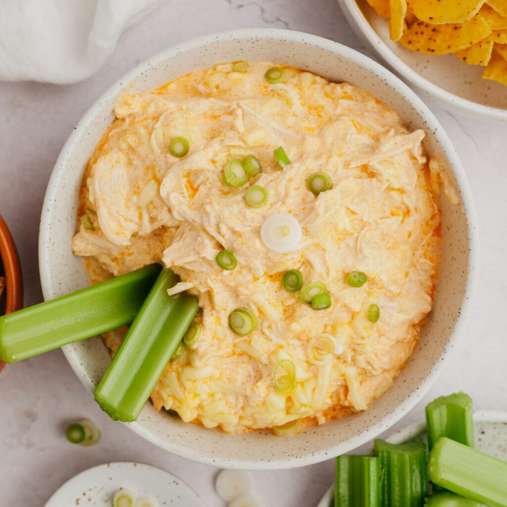 a photo of buffalo chicken dip in a white bowl with two celery sticks dipped into it