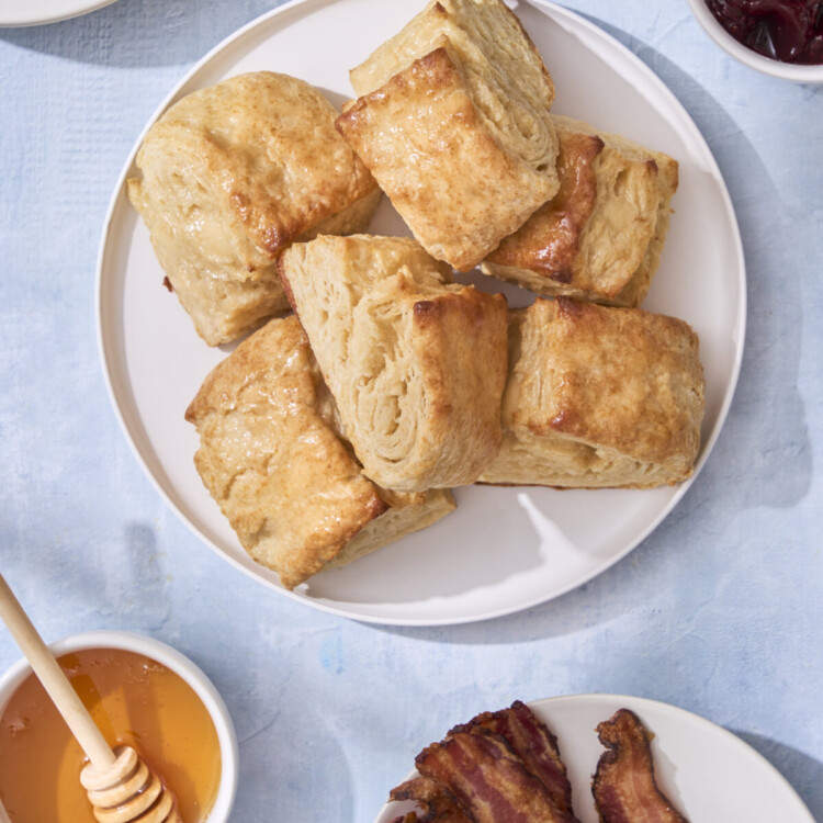 an above image photo of honey butter biscuits on a plate with honey, bacon, and jam around the plate