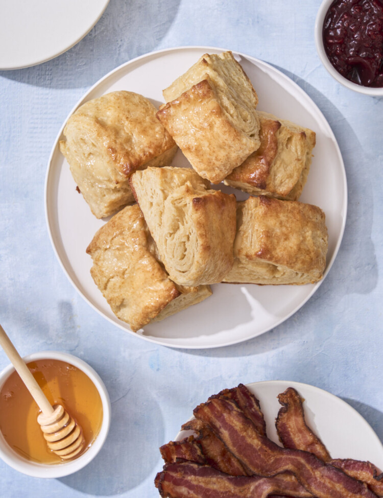 an above image photo of honey butter biscuits on a plate with honey, bacon, and jam around the plate