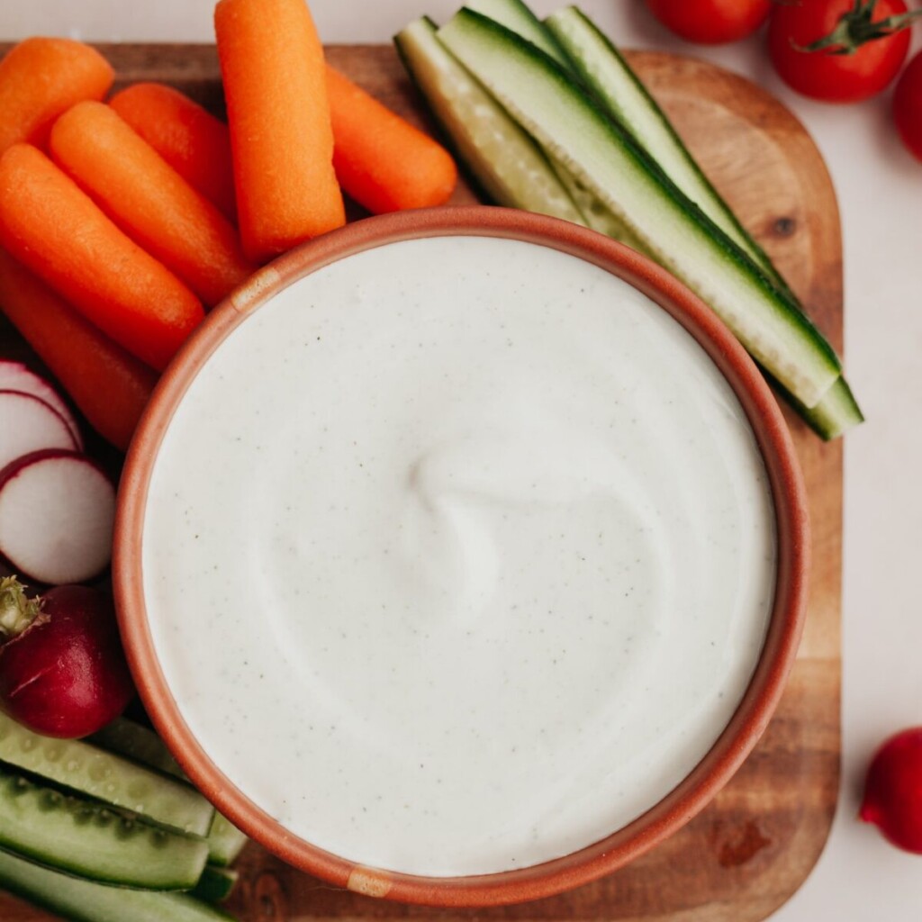 a photo of whipped cottage cheese in a red bowl with carrots, zucchini and radishes around it