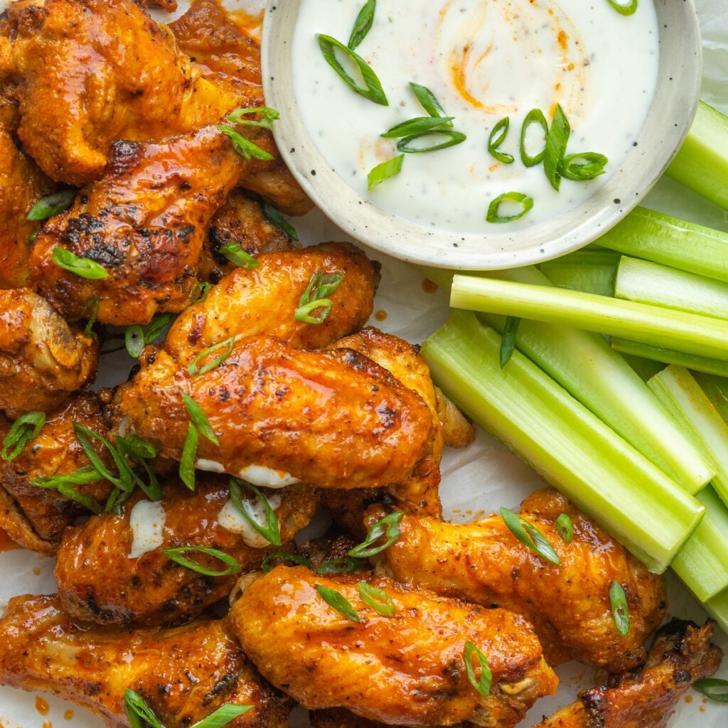 a photo of buffalo wings with a small bowl of ranch and celery with sliced green onions on them