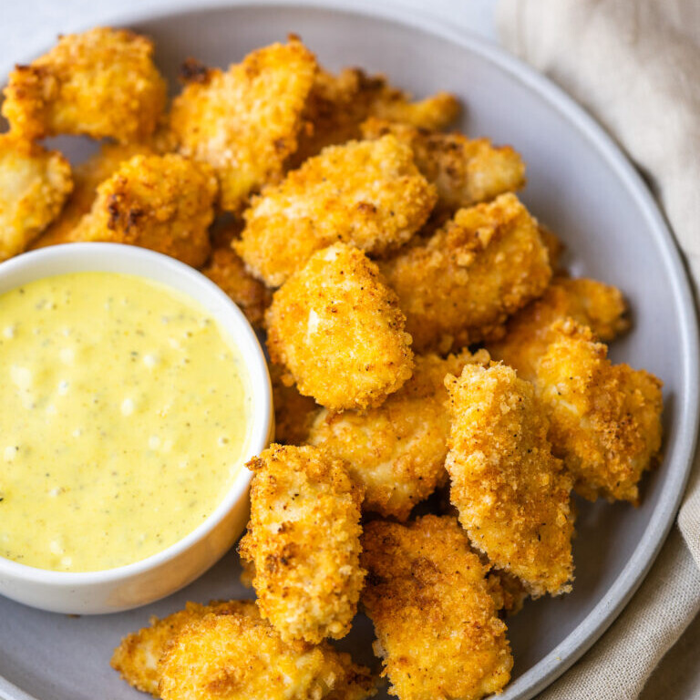 a photo of air fryer popcorn chicken on a gray plate with a bowl of sauce next to it