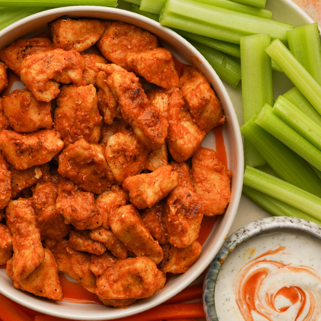 an above view photo of buffalo chicken bites in a white bowl with celery and ranch beside it