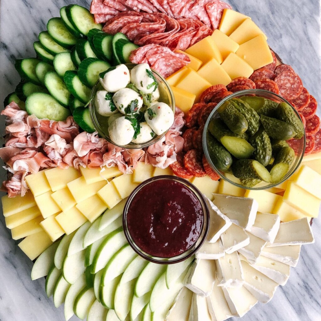 a photo of a charcuterie board with cheese, meat,  jam, and apples