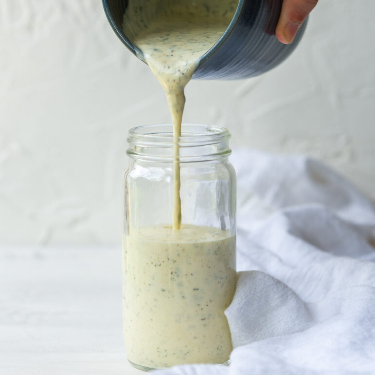 a photo of a hand pouring ranch dressing from a pitcher into a glass jar