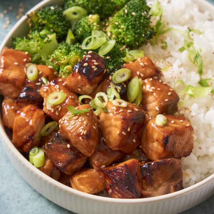 a close up photo of air fryer salmon bites in a white bowl with broccoli and rice and sliced green onions sprinkled on top