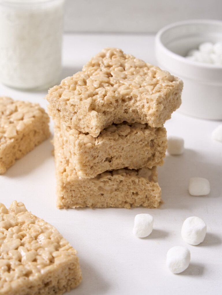 a three quarter view photo of three rice krispie treats stacked on top of each other with a bite taken out of the top one