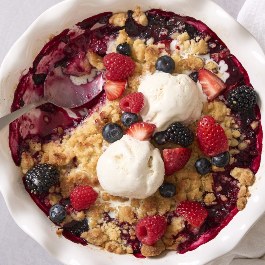 a photo of mixed berry cobbler with ice cream on top in a white dish
