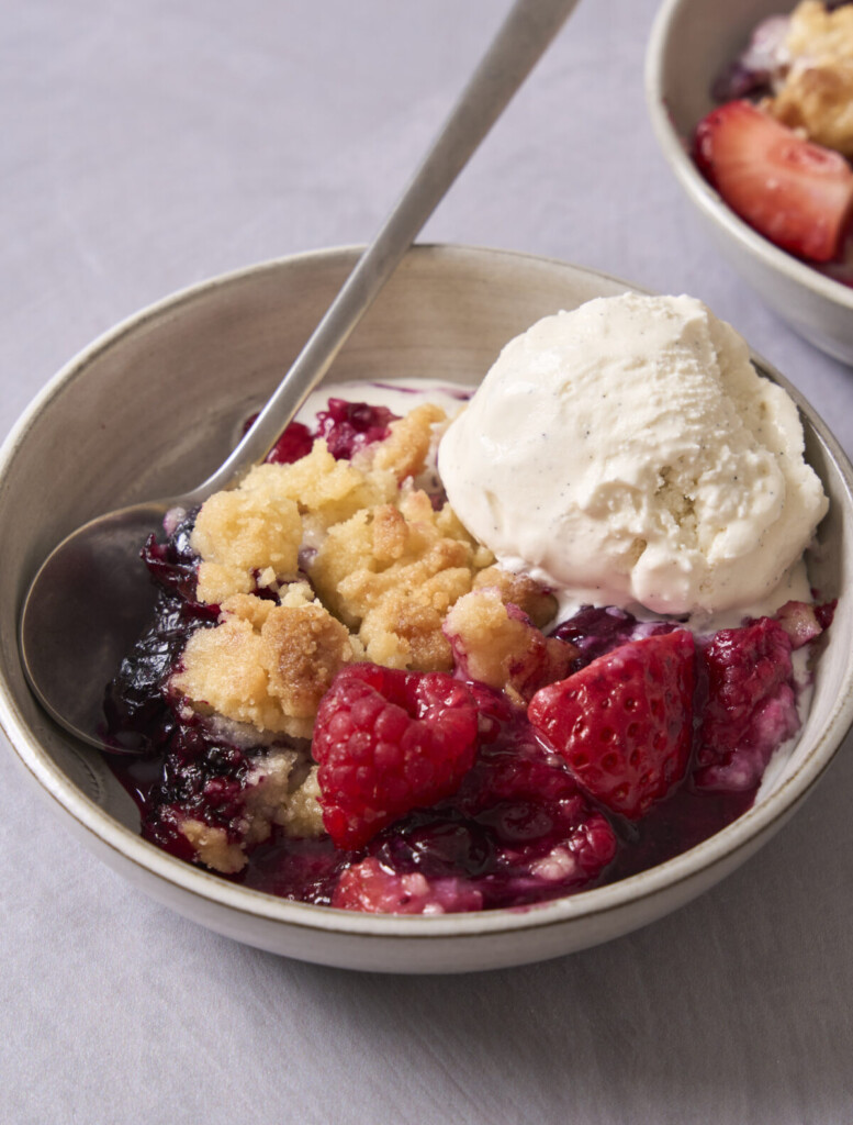 a close up photo of mixed berry cobbler in a bowl with a scoop of ice cream on top