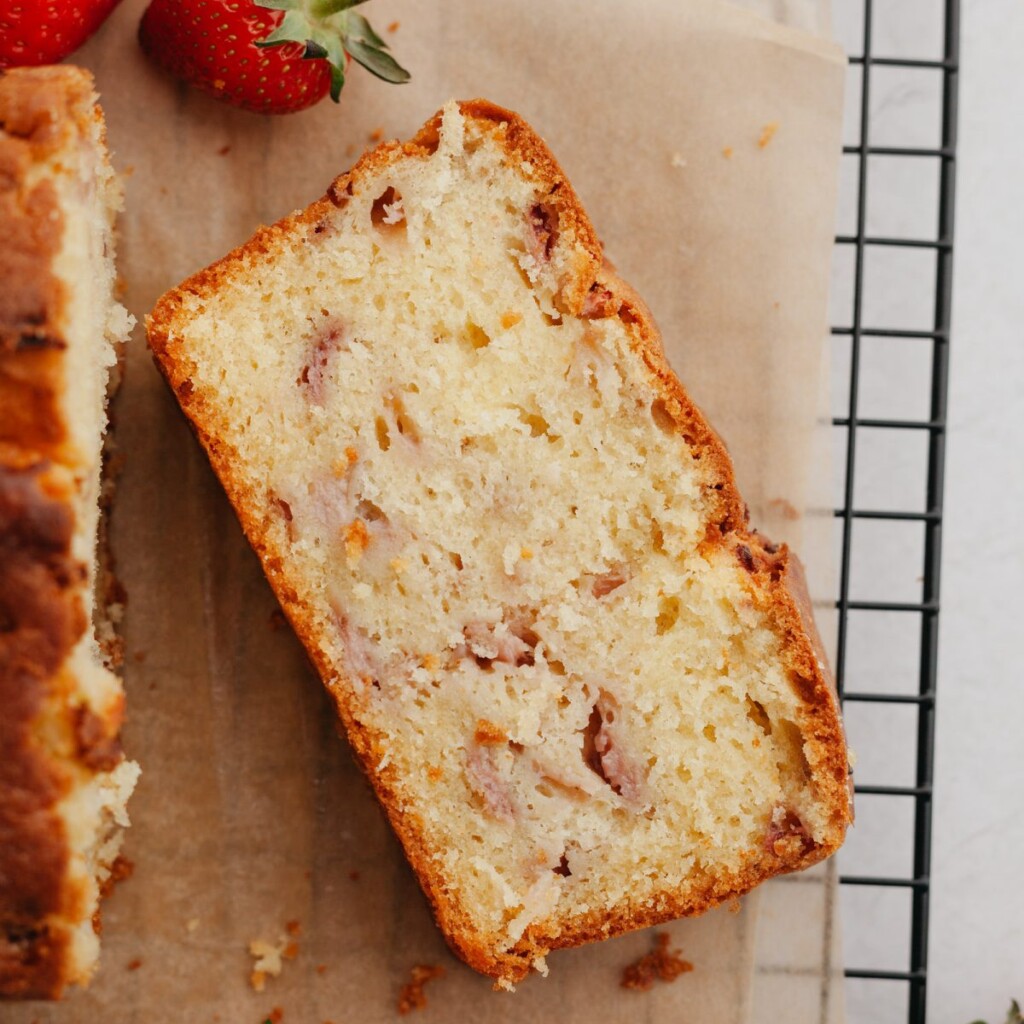 an above view photo of a slice of strawberry pound cake laying on a piece of parchment on a cooling rack